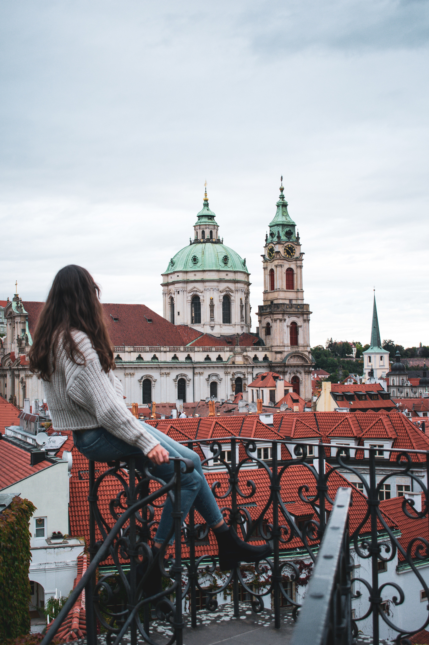 Woman sitting on a fence looking at a church in Prague 