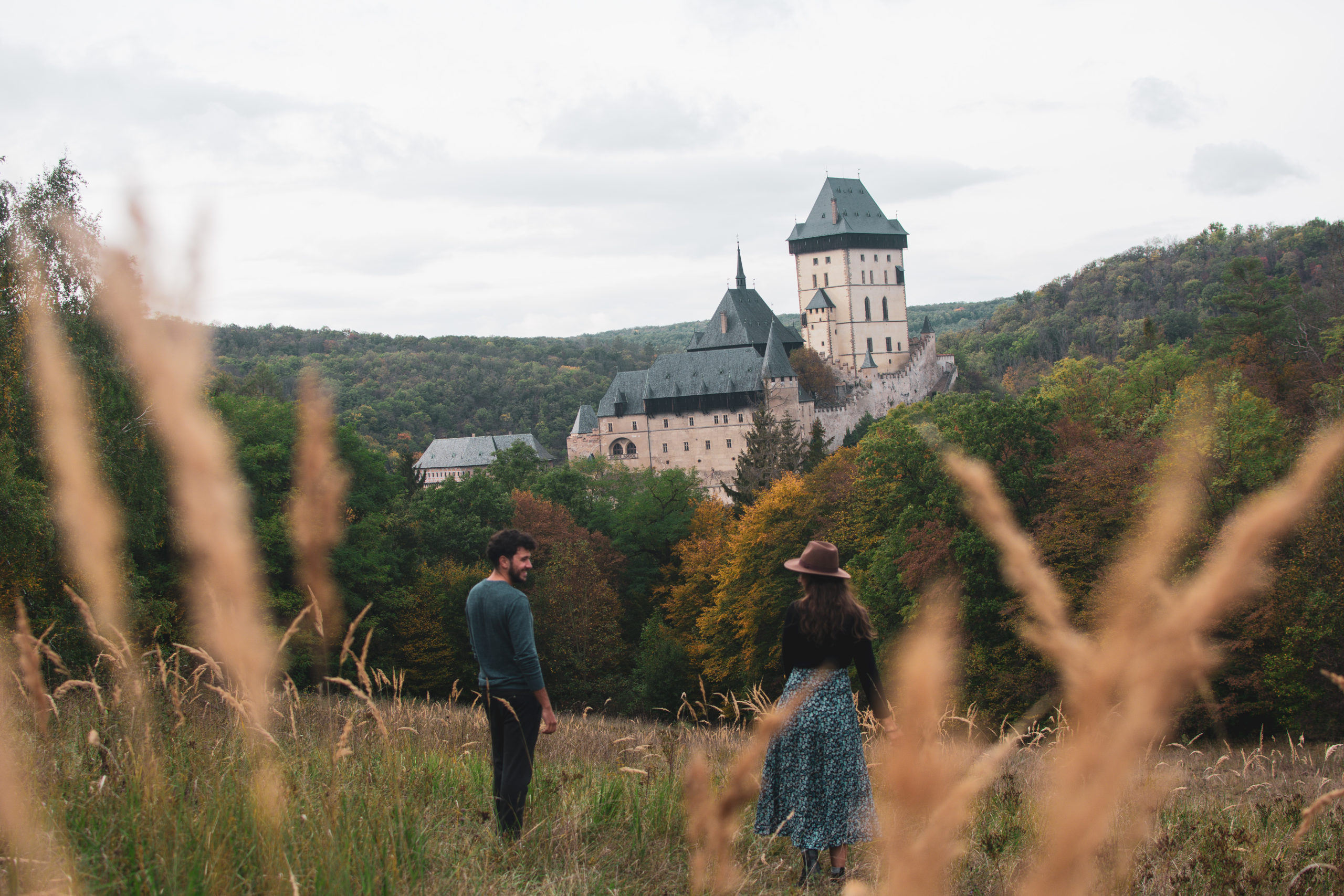 Couple walking in a field with a castle in Czech Republic