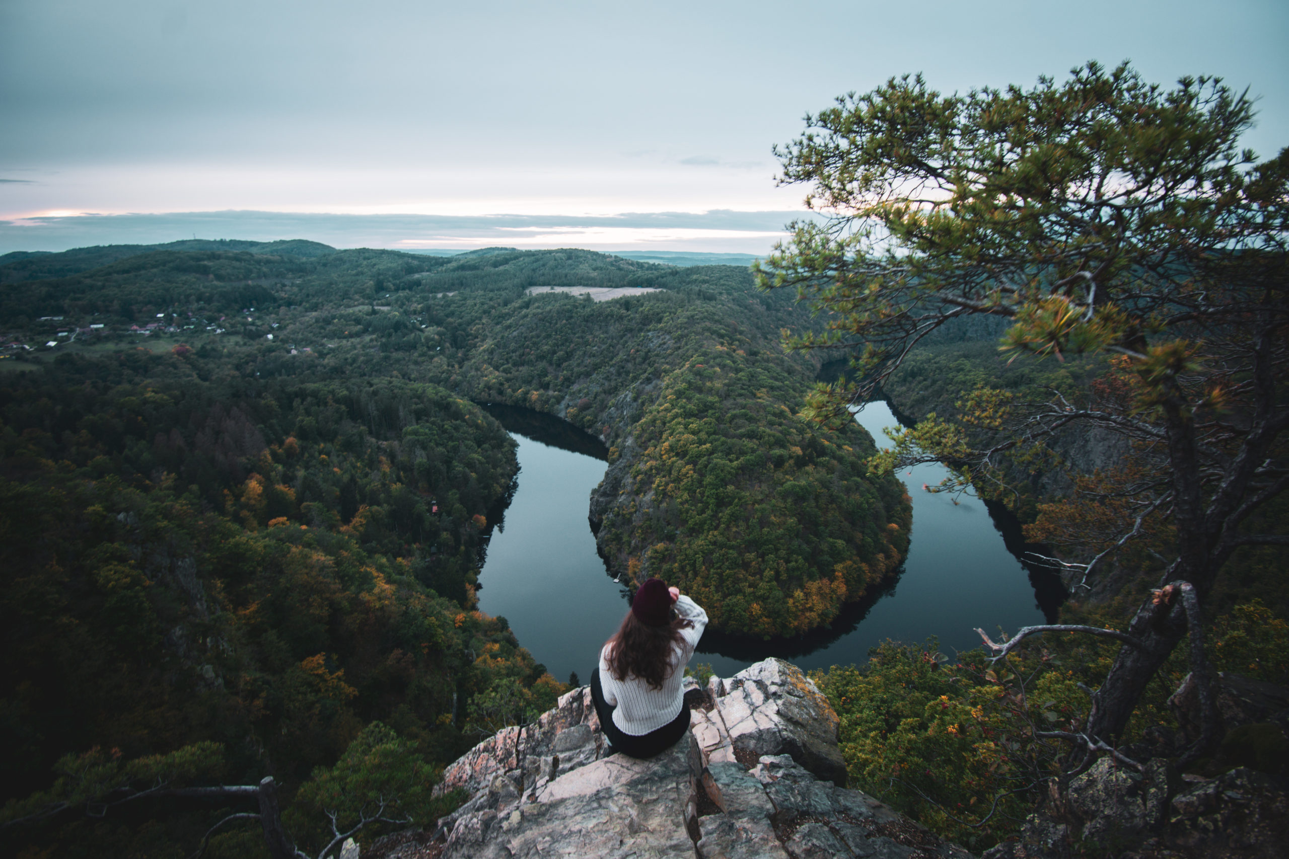 Woman sit in front of Vihlydka Maj, a green horseshoe bend in Czech Republic