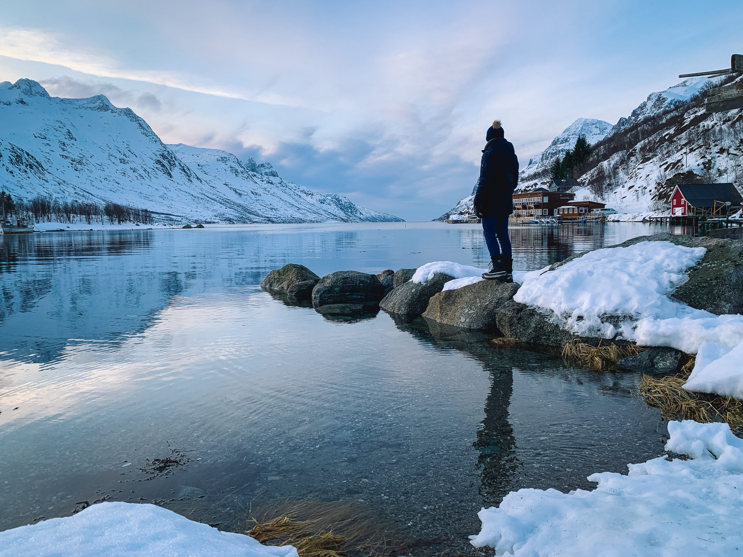 Man standing on snowy rocks in a fjord near Tromsø