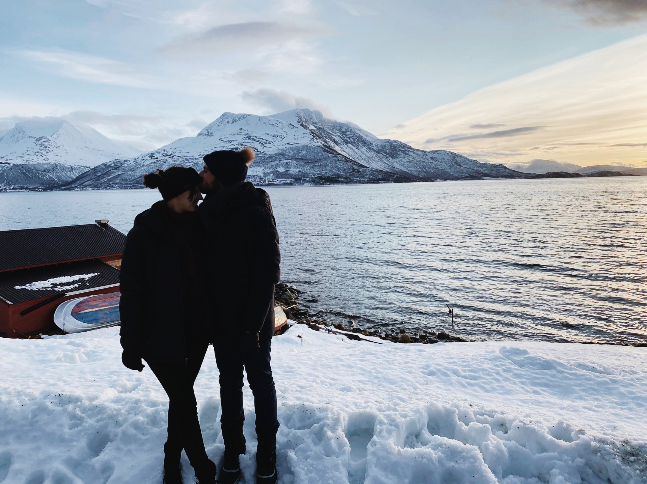 Couple hugging in front of a sunset in a fjord covered with snow in Tromsø
