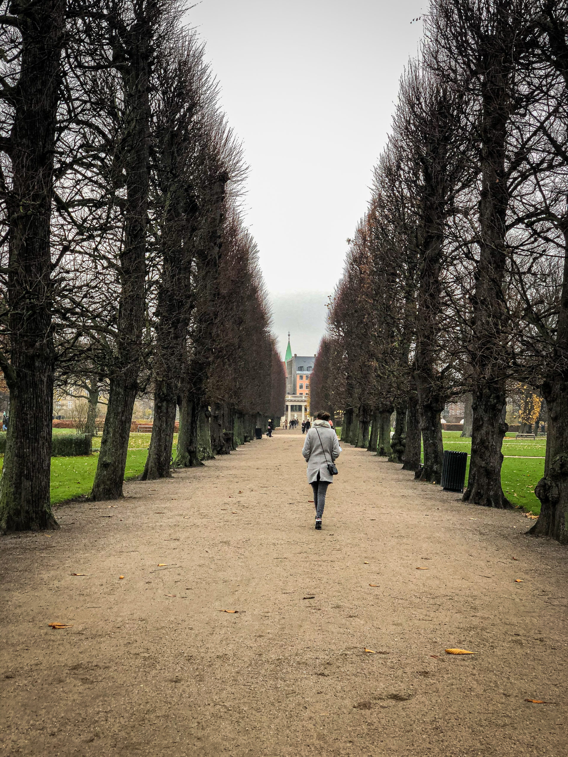 Woman walking in the middle of trees in the Rosenborg Castle in Copenhagen