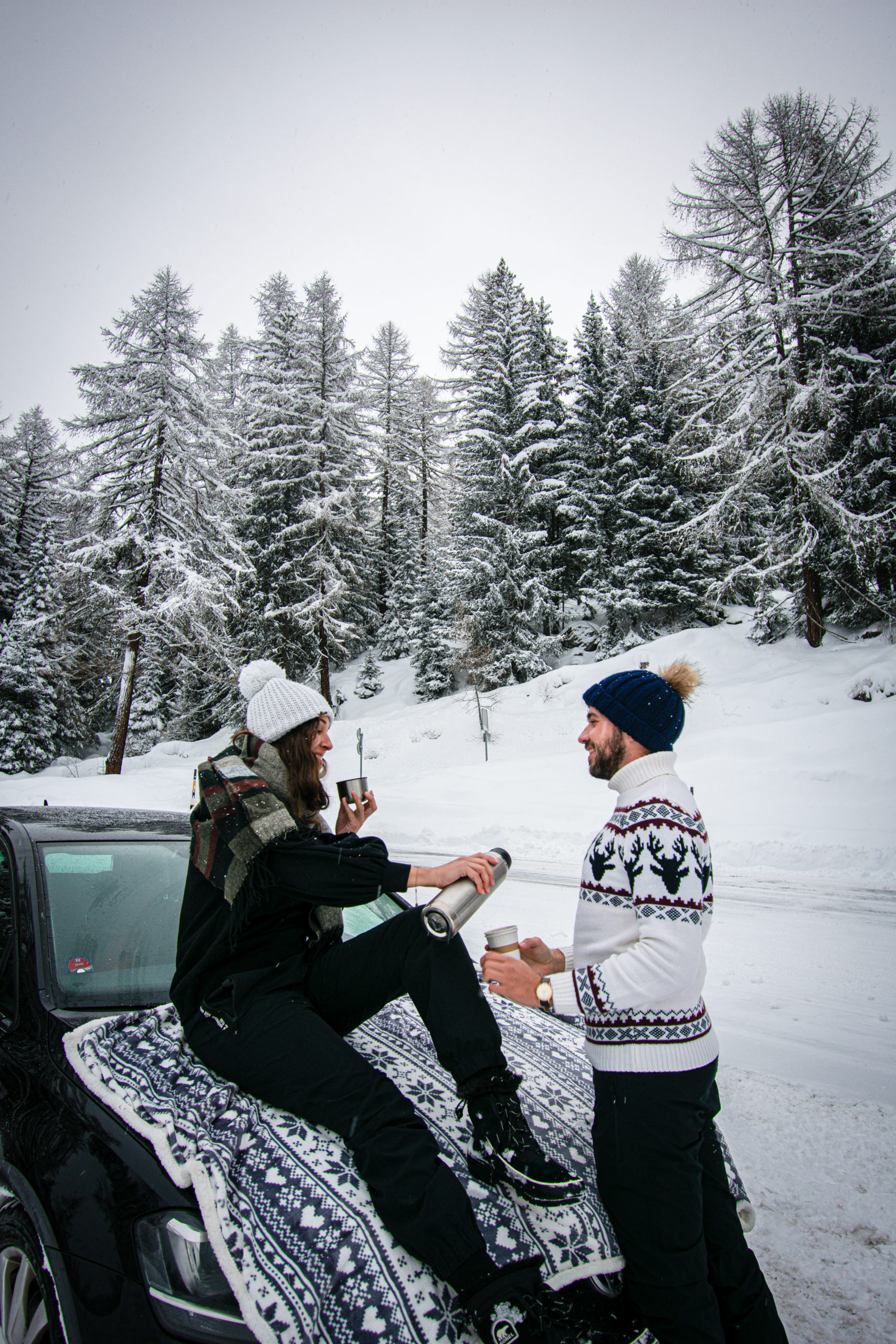 Two people drinking a tea on a car in the snow