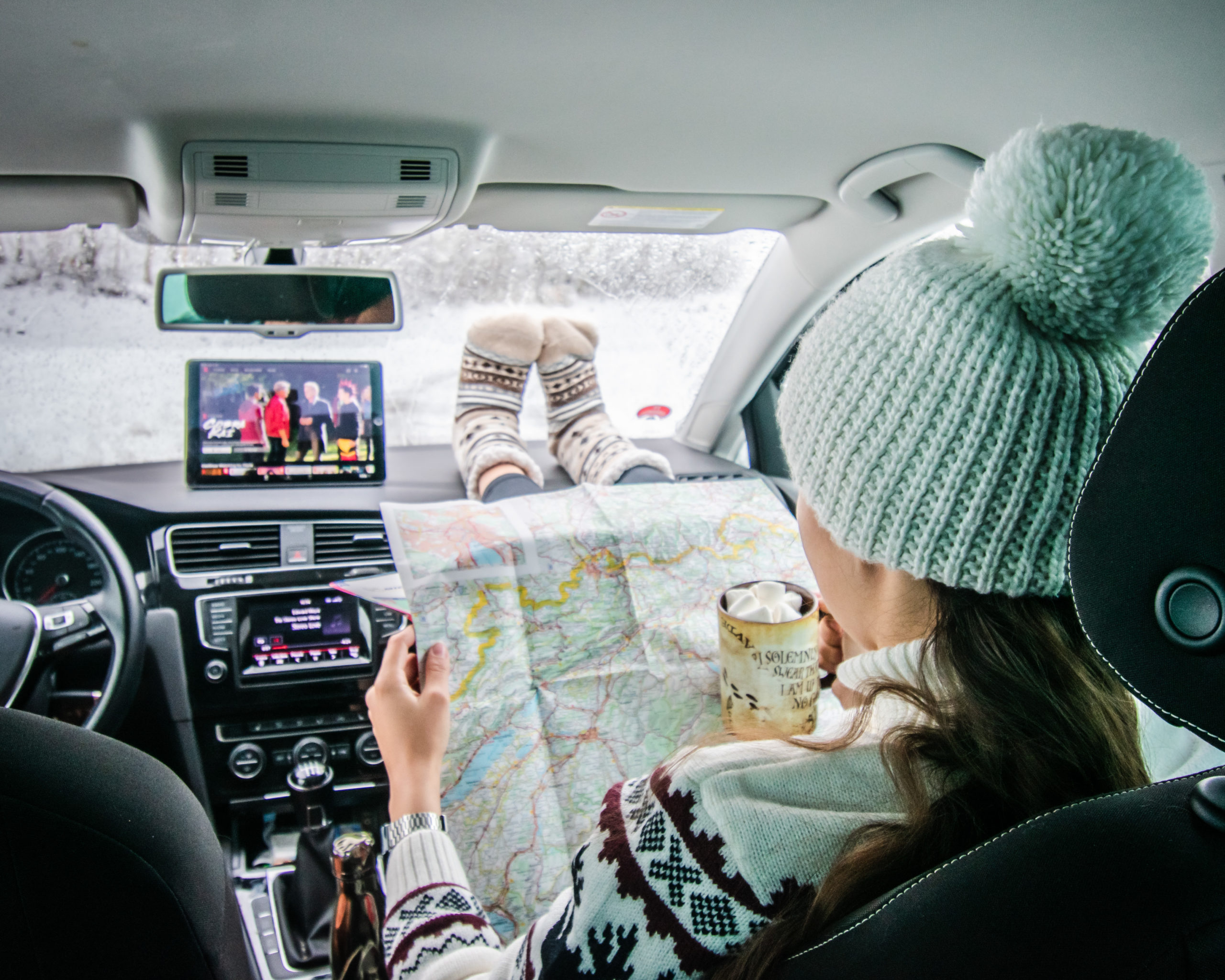 Woman drinking a hot chocolate and looking at a paper map in a car
